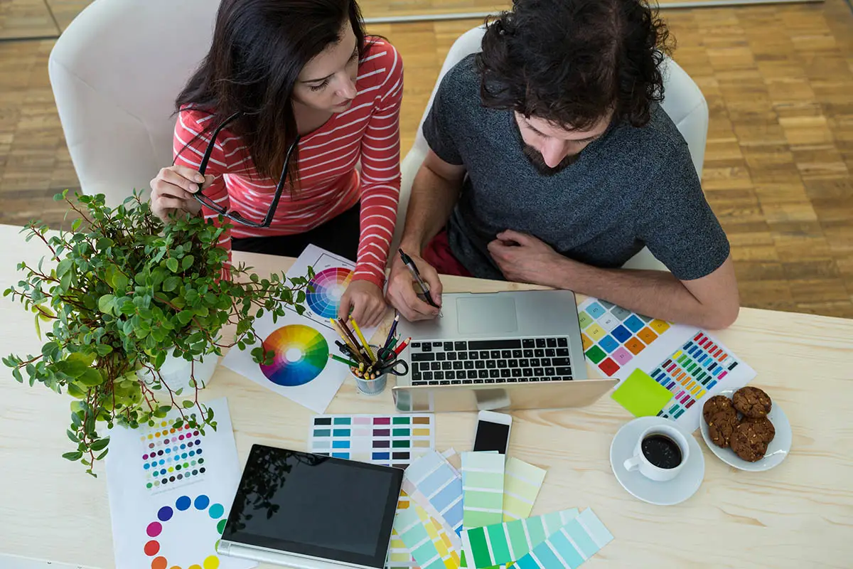 Designers collaborating on branding project with color palettes and laptop.