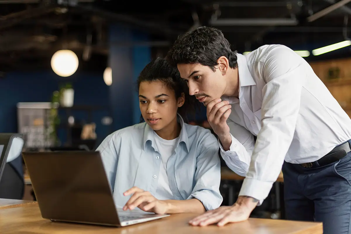 Two professionals collaborating on laptop for social media project development.
